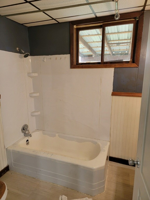 bathroom featuring wooden walls, a drop ceiling, shower / tub combination, and a wealth of natural light