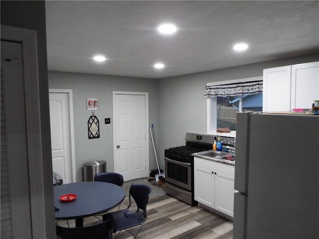 kitchen with sink, stainless steel gas range oven, light hardwood / wood-style floors, fridge, and white cabinets