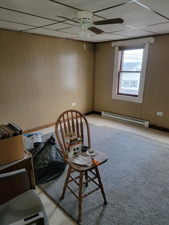 unfurnished room with ceiling fan, wood walls, and a baseboard heating unit