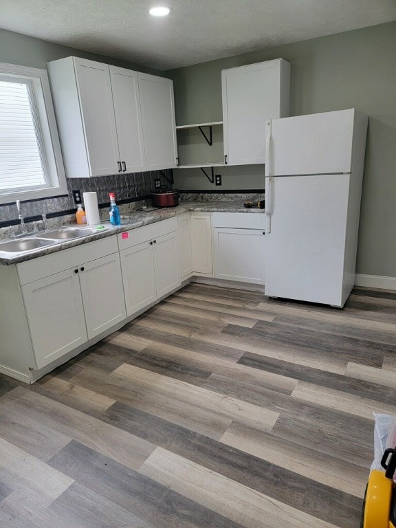 kitchen with light wood-type flooring, white fridge, white cabinetry, and sink