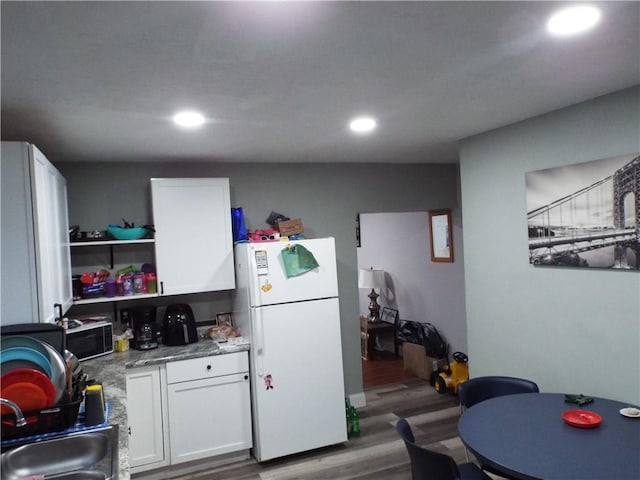 kitchen with light stone countertops, sink, wood-type flooring, white fridge, and white cabinetry