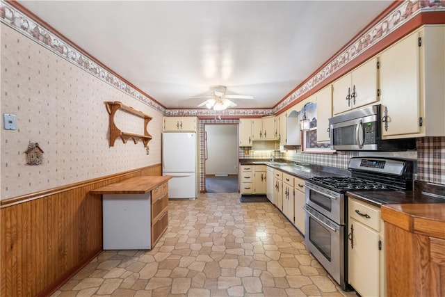 kitchen featuring wooden walls, ceiling fan, cream cabinetry, and appliances with stainless steel finishes