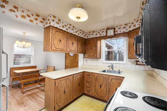 kitchen featuring sink, kitchen peninsula, a chandelier, light hardwood / wood-style floors, and decorative light fixtures