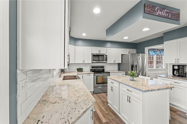 kitchen with hardwood / wood-style floors, a center island, white cabinets, appliances with stainless steel finishes, and light stone counters