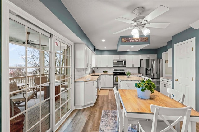 kitchen with white cabinets, light hardwood / wood-style flooring, tasteful backsplash, light stone counters, and stainless steel appliances