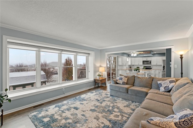 living room featuring crown molding, ceiling fan, a textured ceiling, and light wood-type flooring