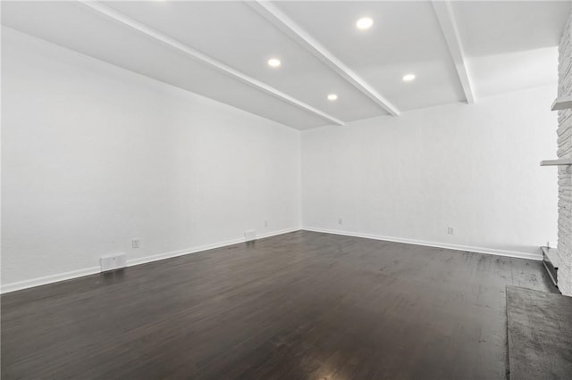 spare room featuring a fireplace, beamed ceiling, and dark wood-type flooring