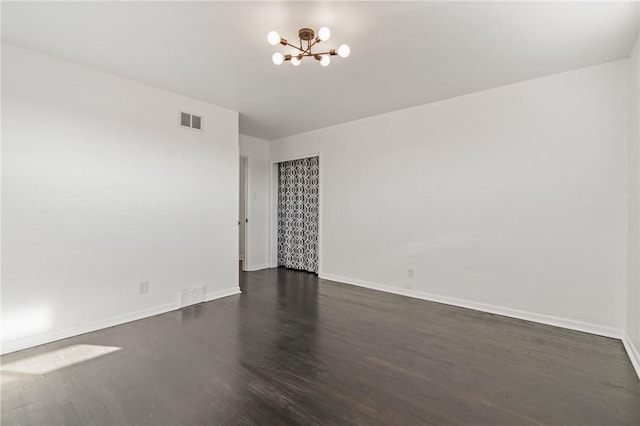 spare room with dark wood-type flooring and a notable chandelier