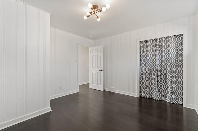 empty room featuring an inviting chandelier and dark wood-type flooring