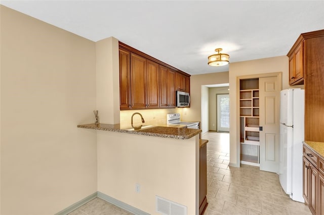 kitchen featuring kitchen peninsula, light stone counters, white appliances, and sink