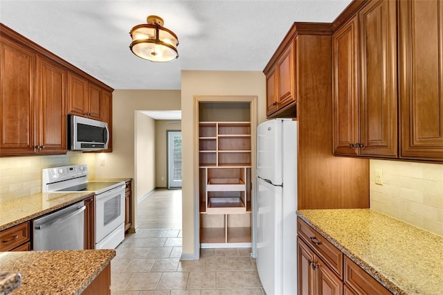 kitchen featuring decorative backsplash, appliances with stainless steel finishes, light stone countertops, and light tile patterned flooring