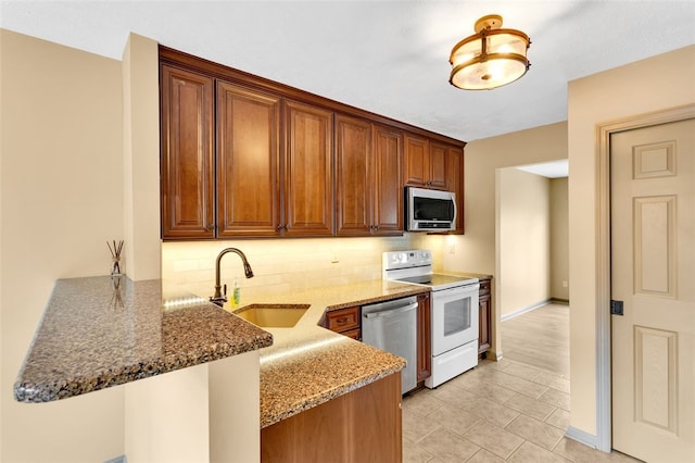 kitchen with sink, decorative backsplash, appliances with stainless steel finishes, stone countertops, and kitchen peninsula