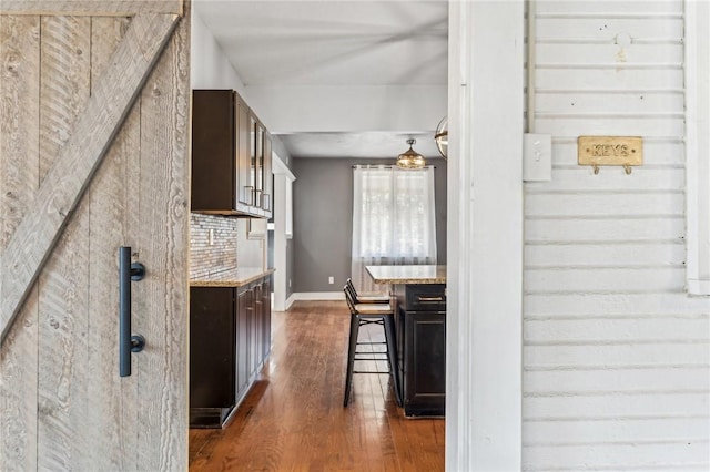 kitchen featuring dark hardwood / wood-style floors, light stone countertops, tasteful backsplash, a kitchen bar, and dark brown cabinetry