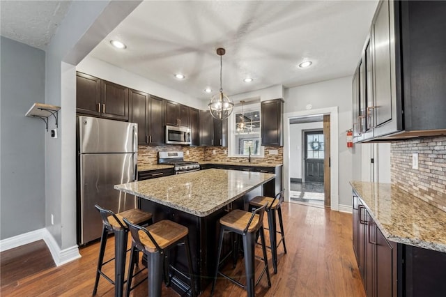 kitchen with dark hardwood / wood-style floors, a kitchen island, decorative light fixtures, and appliances with stainless steel finishes