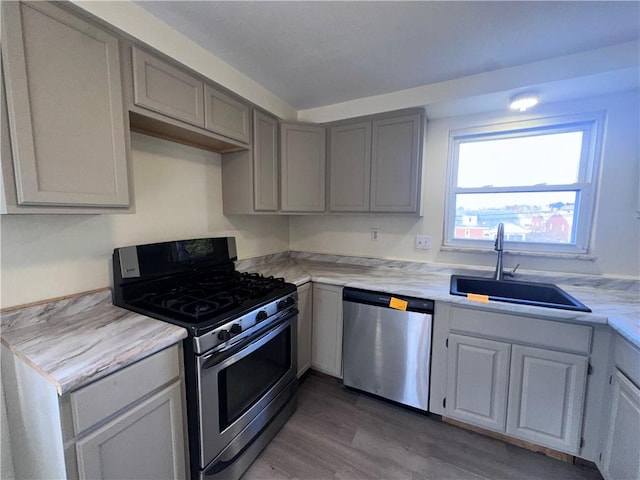 kitchen with appliances with stainless steel finishes, hardwood / wood-style flooring, gray cabinets, and sink