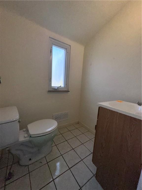 bathroom with tile patterned flooring, vanity, toilet, and lofted ceiling