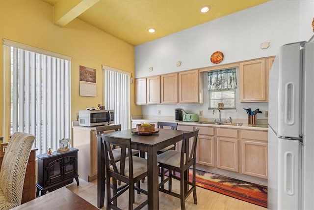 kitchen with sink, white fridge, light brown cabinetry, and beamed ceiling