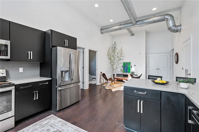 kitchen featuring dark hardwood / wood-style floors, a towering ceiling, stainless steel appliances, and tasteful backsplash