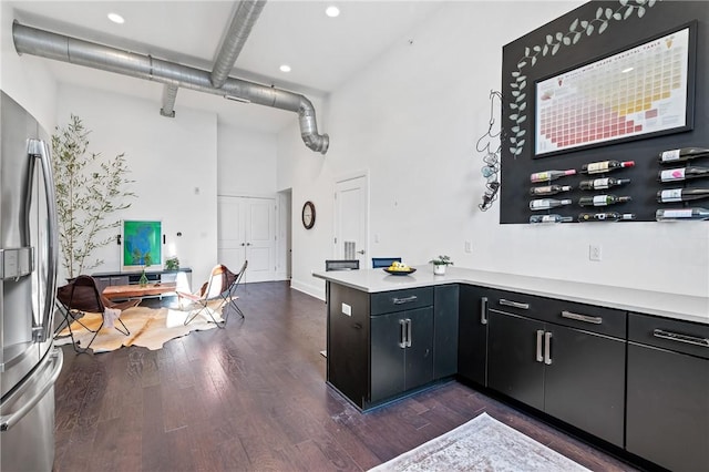 kitchen featuring kitchen peninsula, dark hardwood / wood-style flooring, beamed ceiling, a high ceiling, and stainless steel refrigerator