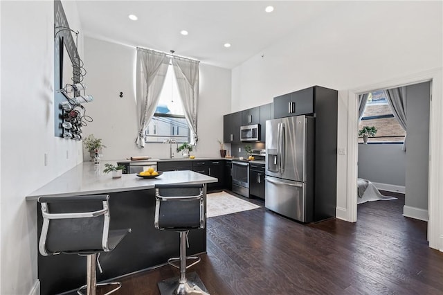 kitchen featuring kitchen peninsula, a kitchen bar, stainless steel appliances, dark wood-type flooring, and sink