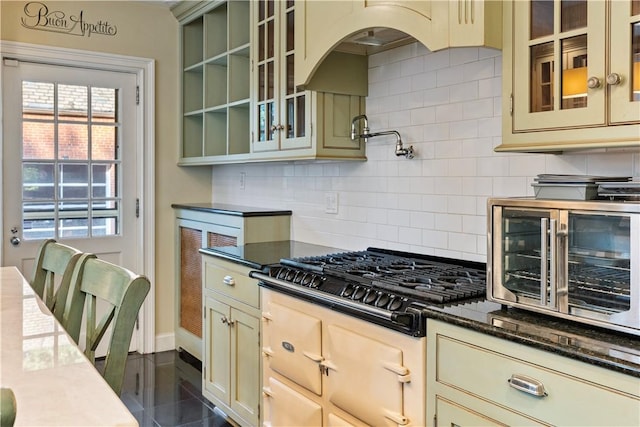 kitchen featuring decorative backsplash, cream cabinetry, dark stone counters, and gas stovetop