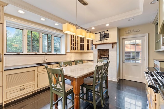 kitchen with a fireplace, crown molding, sink, cream cabinetry, and hanging light fixtures