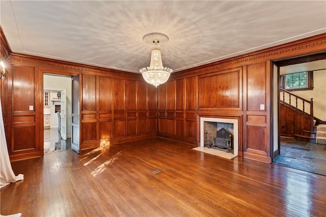 unfurnished living room with wooden walls, ornamental molding, a notable chandelier, and hardwood / wood-style flooring