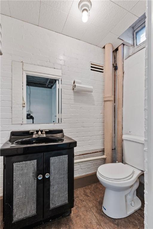 bathroom with tile patterned floors, vanity, toilet, and brick wall