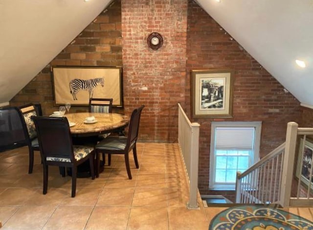 tiled dining room featuring brick wall and lofted ceiling