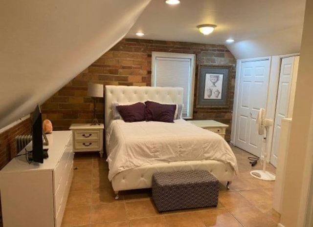 bedroom with light tile patterned floors, lofted ceiling, and brick wall