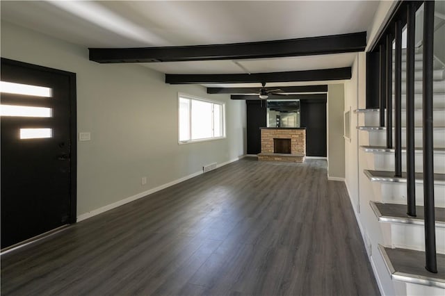 unfurnished living room with beam ceiling, dark hardwood / wood-style flooring, a brick fireplace, and ceiling fan