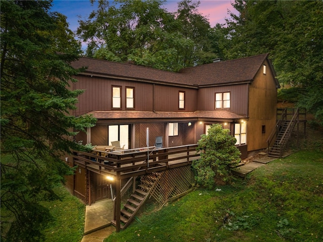 back house at dusk featuring a wooden deck and a yard