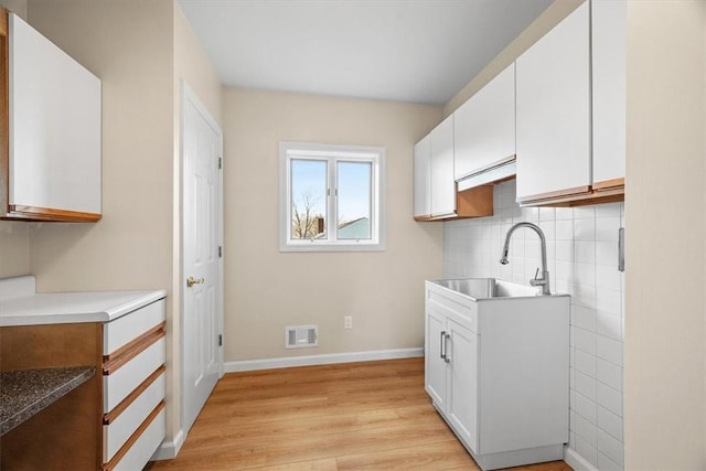 kitchen with decorative backsplash, sink, white cabinets, and light wood-type flooring