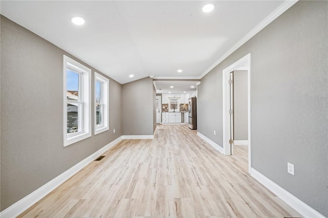 unfurnished living room with vaulted ceiling, crown molding, and light hardwood / wood-style flooring