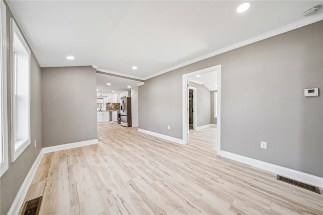 unfurnished living room featuring crown molding and light wood-type flooring