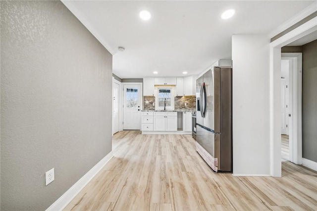 kitchen with appliances with stainless steel finishes, tasteful backsplash, sink, white cabinets, and light hardwood / wood-style floors