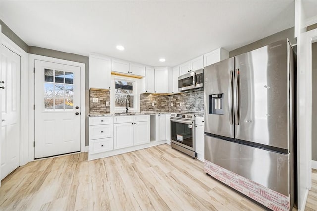 kitchen featuring sink, tasteful backsplash, light hardwood / wood-style floors, white cabinetry, and stainless steel appliances