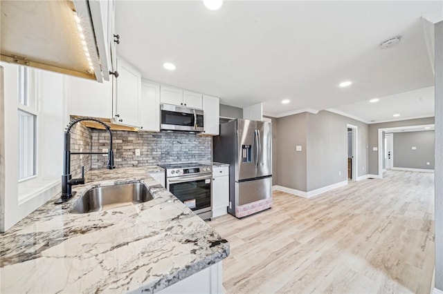 kitchen with light stone countertops, sink, stainless steel appliances, white cabinets, and light wood-type flooring