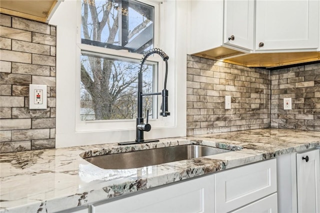 kitchen featuring white cabinets, decorative backsplash, light stone countertops, and sink