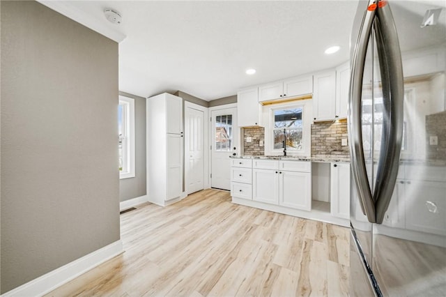 kitchen featuring white cabinets, decorative backsplash, light wood-type flooring, and stainless steel refrigerator