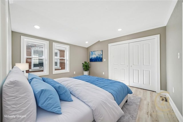 bedroom with a closet, light hardwood / wood-style floors, lofted ceiling, and ornamental molding