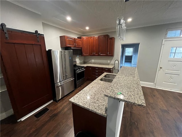 kitchen with a kitchen island with sink, sink, a barn door, appliances with stainless steel finishes, and dark hardwood / wood-style flooring