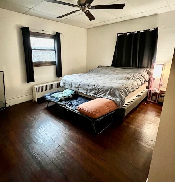 bedroom featuring radiator heating unit, dark hardwood / wood-style flooring, ceiling fan, and a paneled ceiling