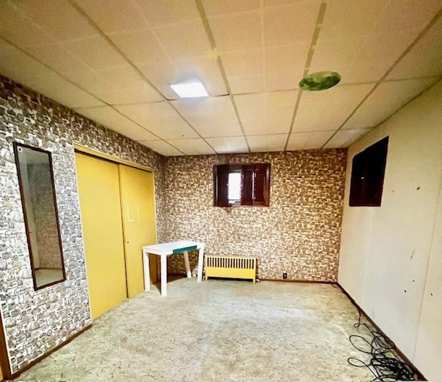 basement with carpet, radiator heating unit, and a paneled ceiling