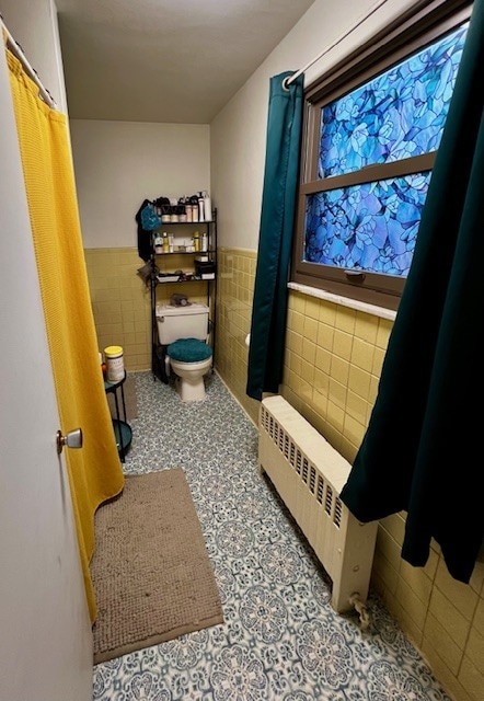 bathroom featuring radiator, tile walls, and toilet