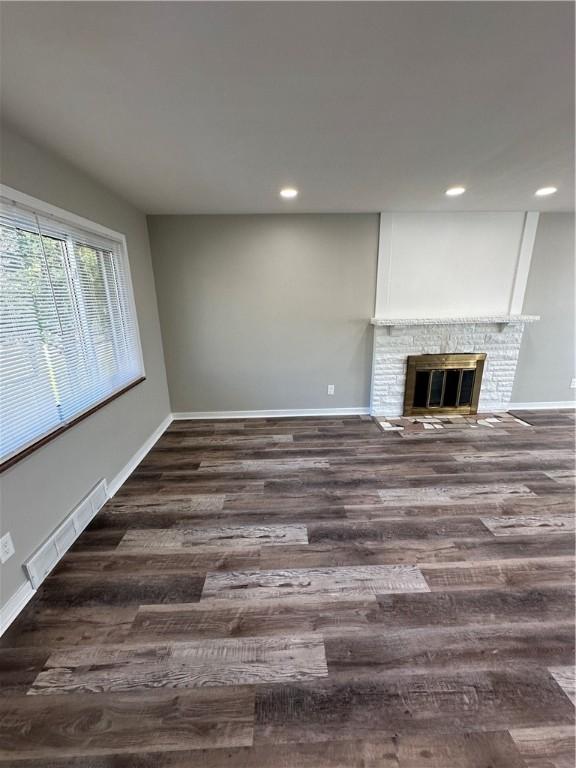 unfurnished living room with dark wood-type flooring and a brick fireplace