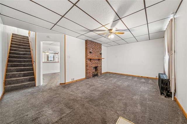 unfurnished living room with a paneled ceiling, ceiling fan, dark colored carpet, and a brick fireplace