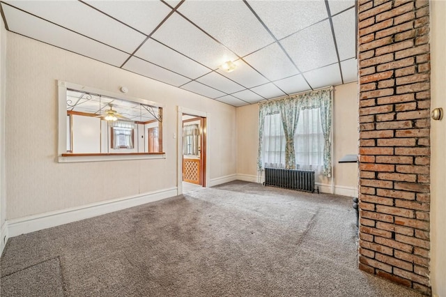 unfurnished living room featuring carpet flooring, radiator heating unit, a drop ceiling, and ceiling fan