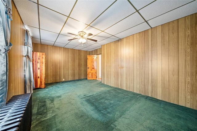 carpeted empty room with ceiling fan and wood walls