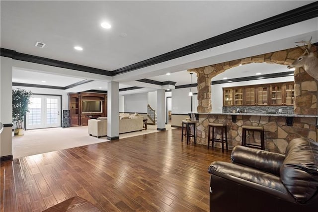 living room with hardwood / wood-style floors, indoor bar, ornate columns, and crown molding